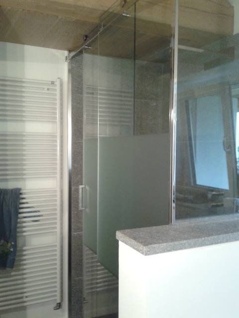 Box doccia con vetro smerigliato, piano in pietra grigia e radiatore bianco.