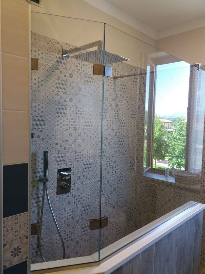 Box doccia in vetro con soffione a pioggia, piastrelle decorate e finestra.