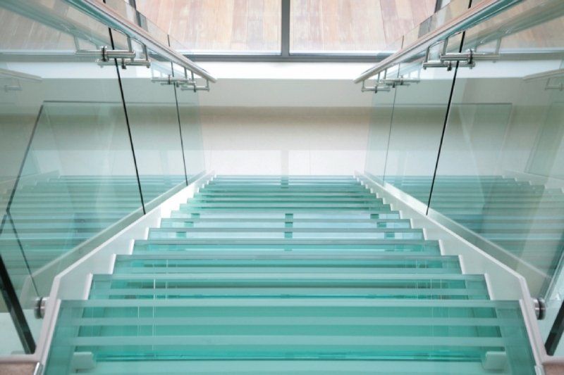 Scala in vetro, gradini azzurri, corrimano laterali in vetro, corrimano in acciaio inox, ambiente interno.