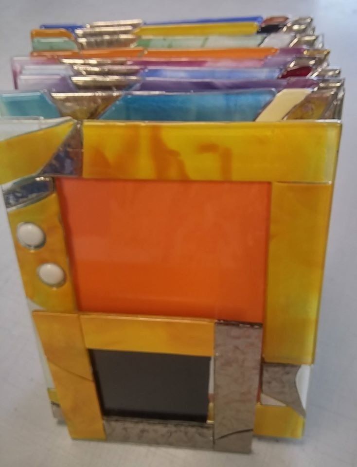 Pila di cornici per foto in vetro colorato e astratto nelle tonalità del giallo, arancione, blu e viola.