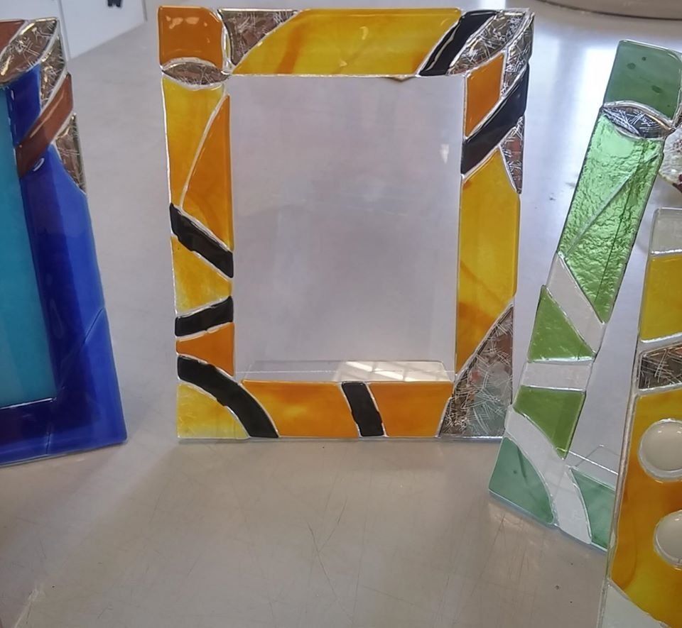 Cornici portafoto in vetro colorato su un tavolo. La cornice centrale è arancione, con dettagli neri e argento.