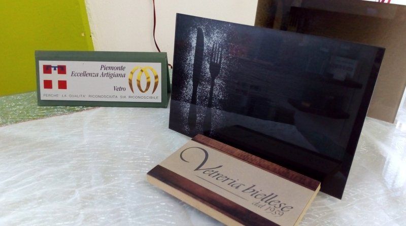 Tre targhe: una verde con uno stemma, una nera lucida e una in simil-legno con del testo.