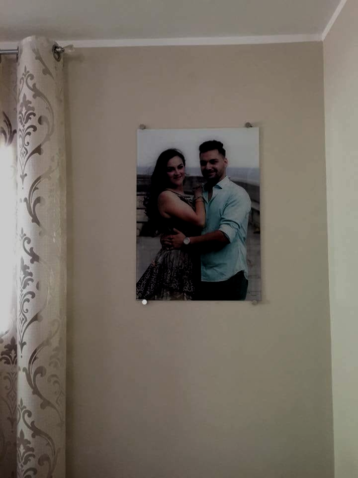 Coppia abbracciata e sorridente nella foto sul muro; abito verde chiaro e floreale.