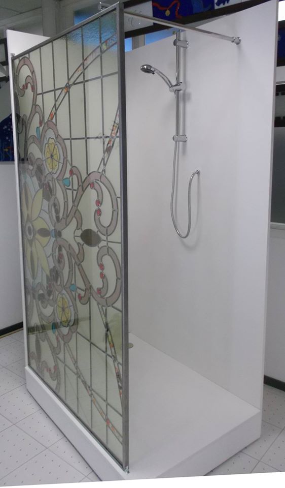 Box doccia con pannello in vetro colorato e soffione argentato. Pareti e base bianche.