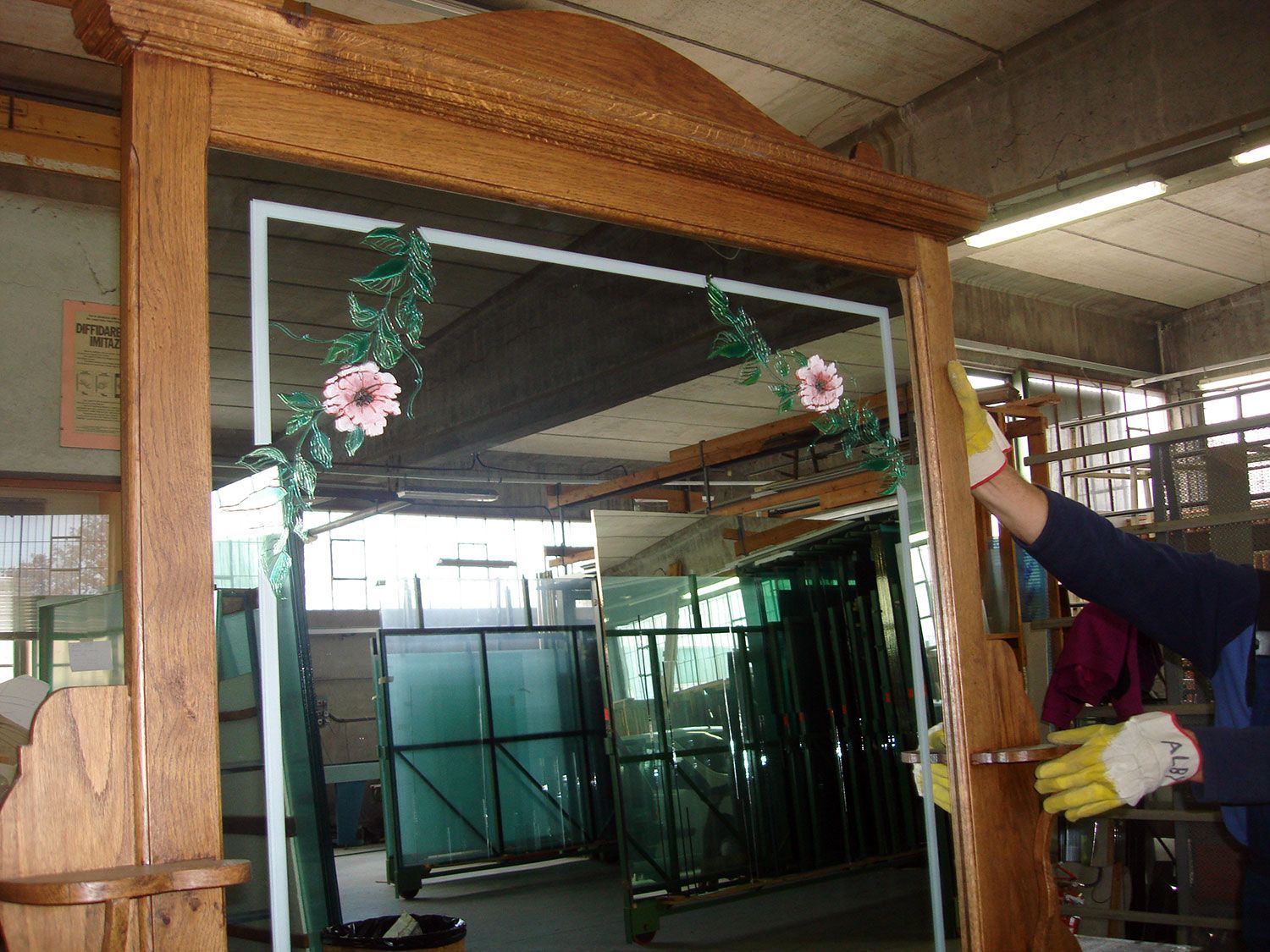 Una persona con i guanti assembla uno specchio con cornice in legno decorato con un motivo floreale dipinto in un laboratorio.