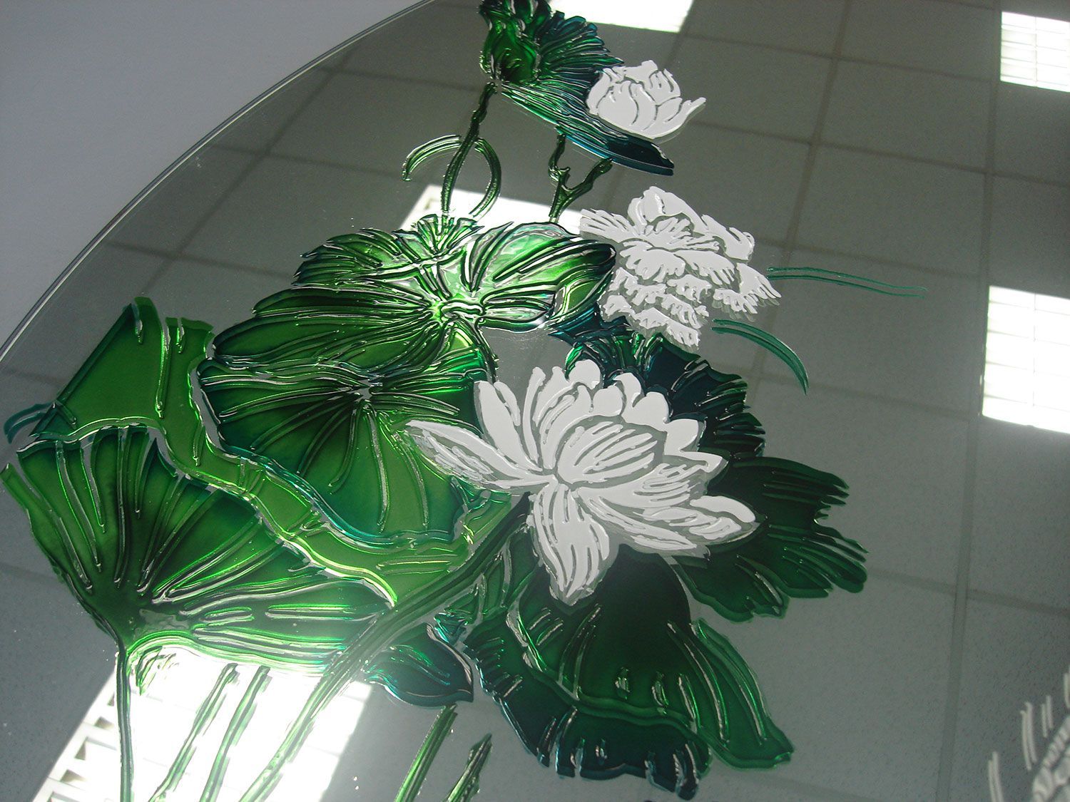 Fiori di loto e foglie in vetro verde su uno specchio; fiori bianchi, illuminati dal sole.