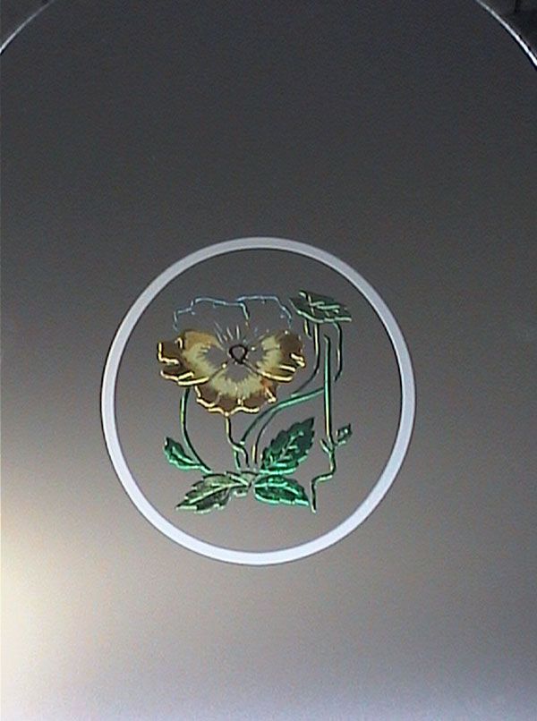 Disegno floreale in rilievo all'interno di un cerchio bianco su sfondo grigio.