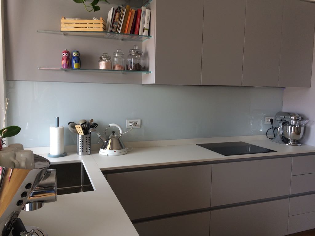 Cucina moderna con mobili grigi, ripiani bianchi e paraschizzi azzurro.