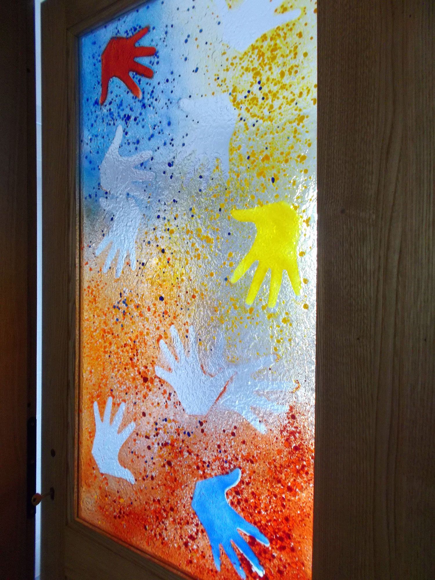 Porta con mani dipinte di rosso, giallo, blu e bianco su uno sfondo colorato e schizzato.