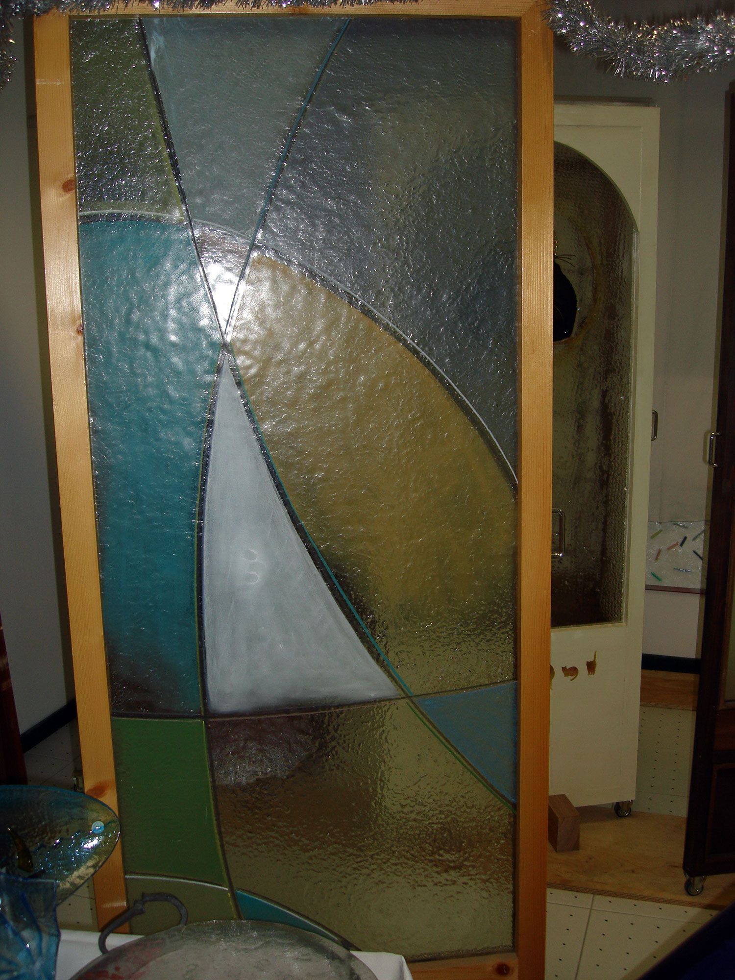 Pannello in vetro colorato con disegno di una barca a vela, verde acqua, oro e bianco. Cornice in legno.