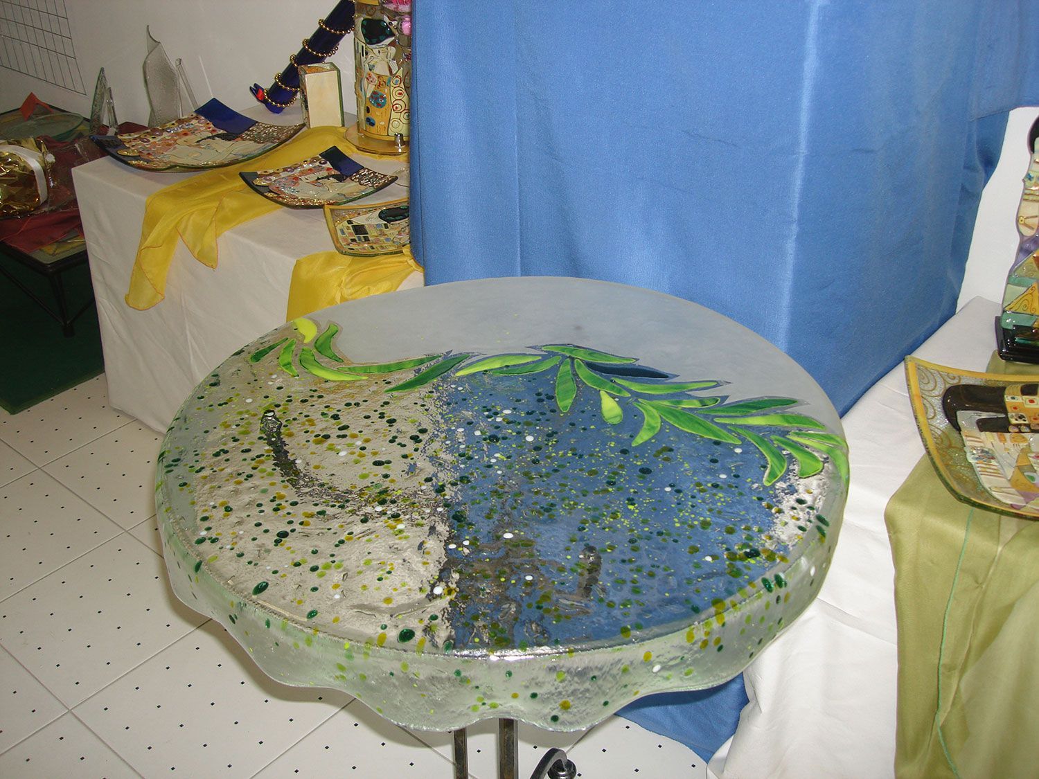 Ciotola artistica in vetro con motivi verdi e blu, esposta in una mostra d'arte.