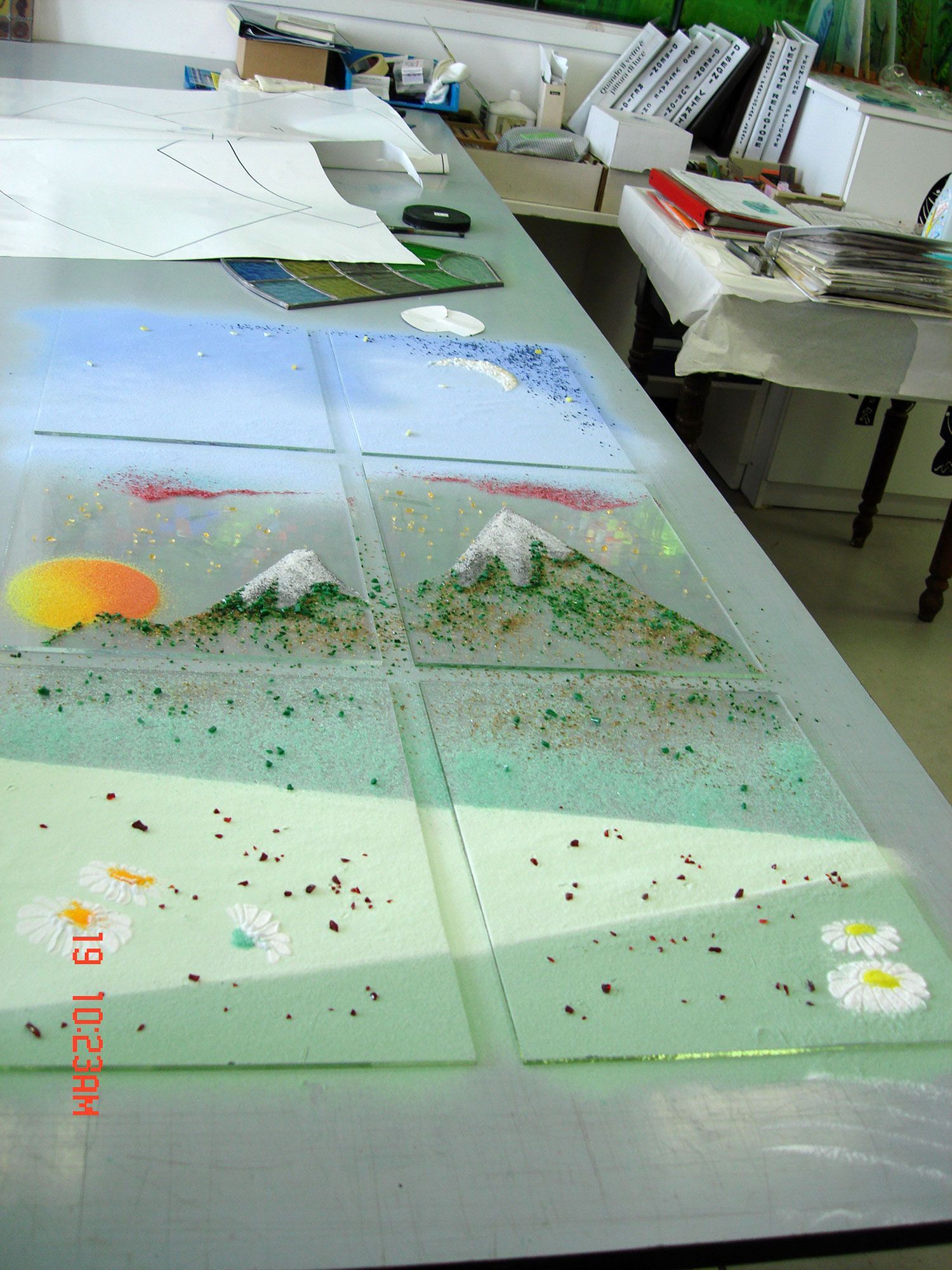 Pannelli di vetro con un disegno paesaggistico: montagne, sole, nuvole e fiori. In un ambiente di laboratorio.