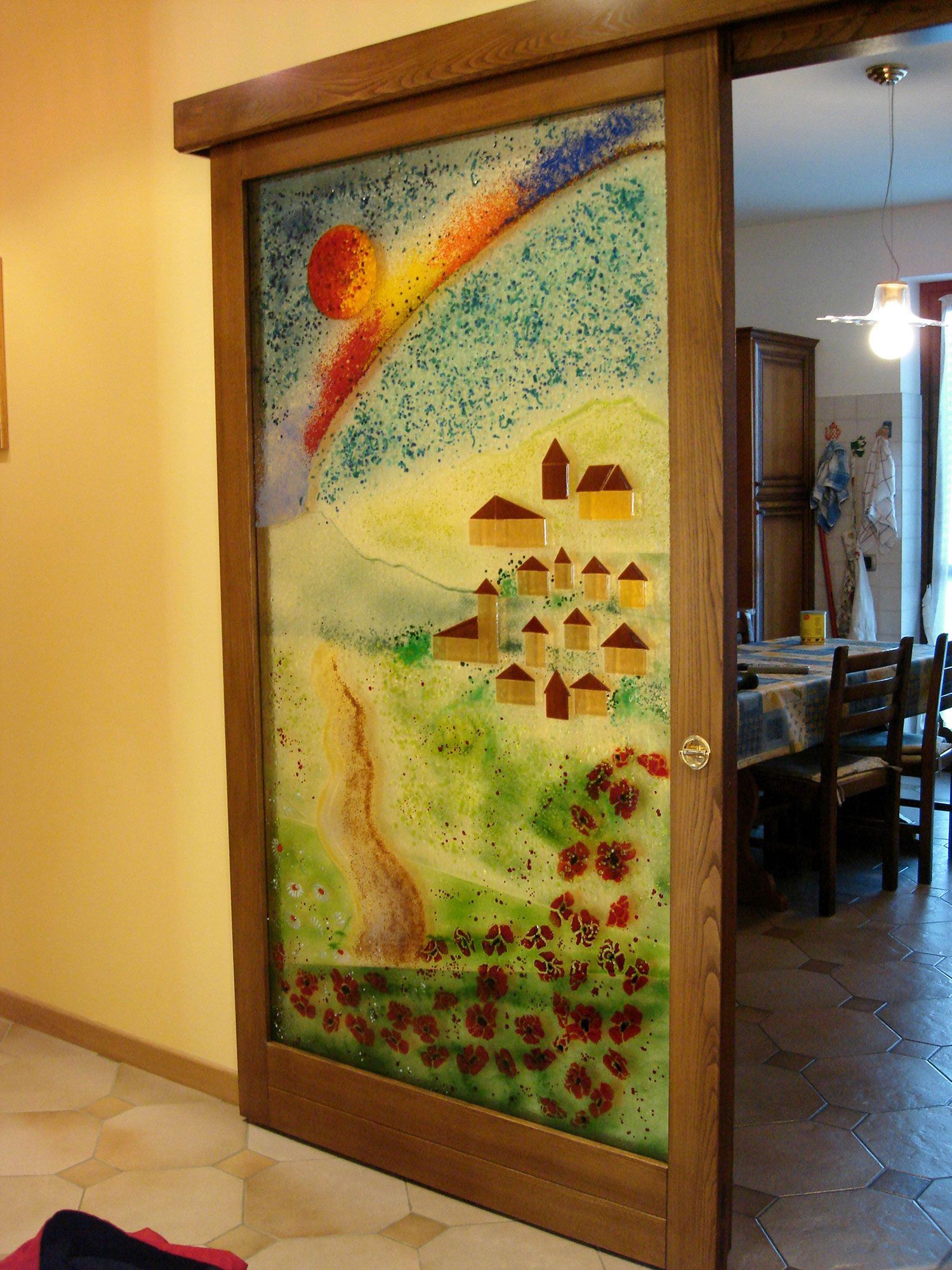 Porta scorrevole in vetro con vetrata raffigurante un villaggio sotto un arcobaleno, incorniciata in legno.