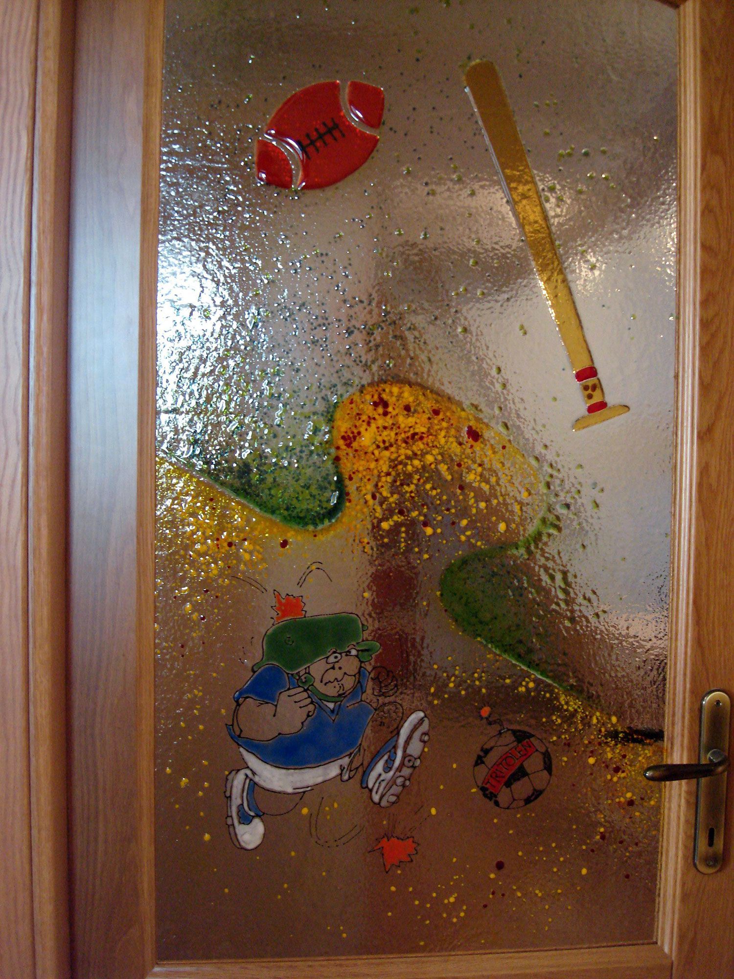 Porta con opere d'arte in vetro a tema sportivo: pallone da football, mazza da baseball, pallone da calcio e un personaggio dei cartoni animati che corre in un cortile.