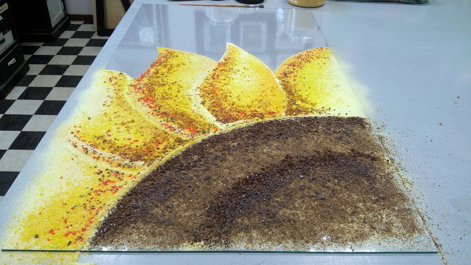 Superficie in vetro con glitter dorati, gialli e marroni che formano montagne stilizzate e un sole.