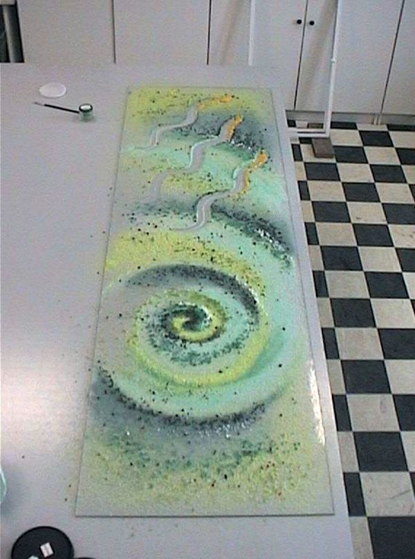 Arte del vetro: una spirale verde con motivi ondulati gialli e bianchi, punteggiati di nero e verde su un tavolo.