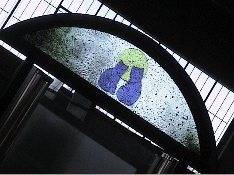 Finestra ad arco con motivo a vetrata: un cerchio giallo con forme blu a forma di guanto su uno sfondo punteggiato.