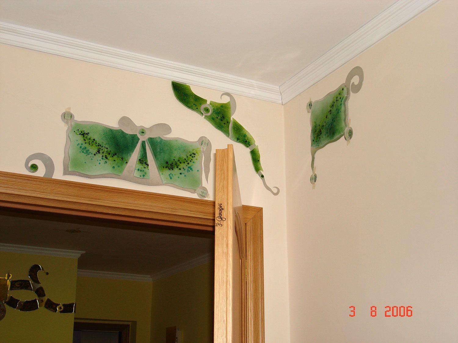 Opera d'arte in vetro verde e bianco su una parete beige, sopra una porta.