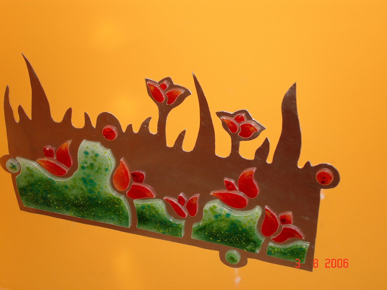 Opera d'arte floreale in metallo marrone con fiori rossi e accenti verdi su sfondo arancione.