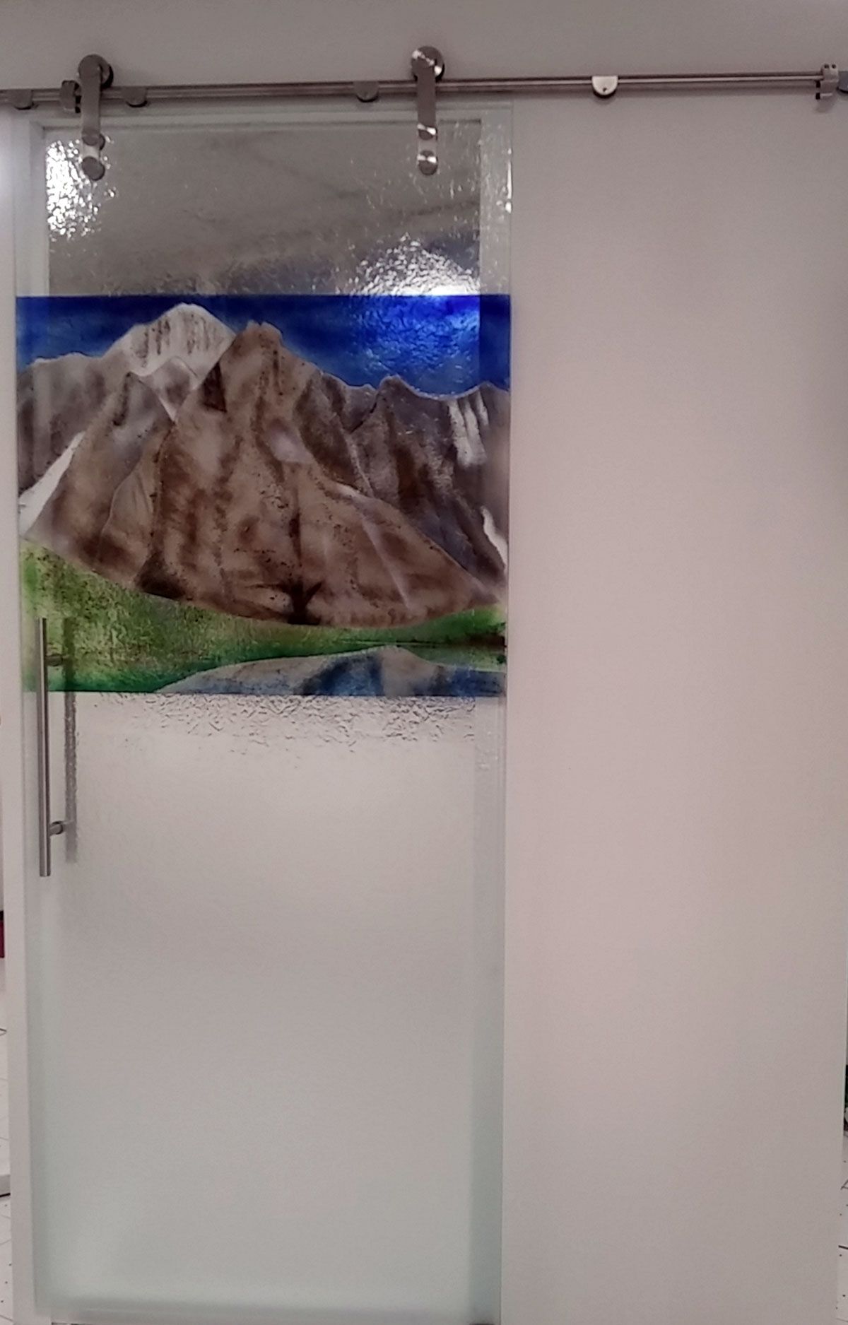 Porta scorrevole in vetro con motivo di montagne. La porta è satinata e dotata di binario in acciaio inox.