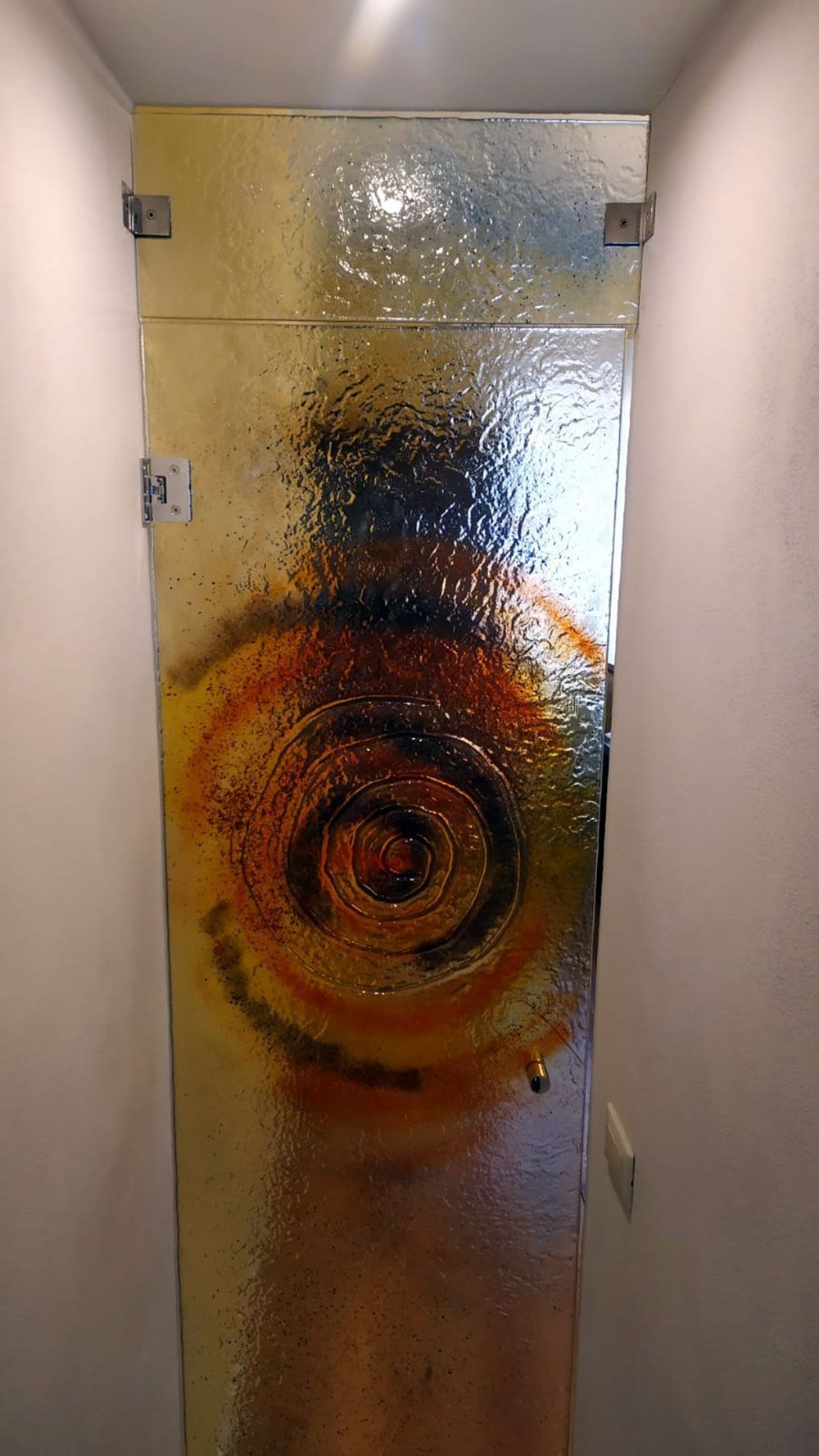 Porta in vetro con un motivo a spirale giallo-arancio, tra pareti bianche.