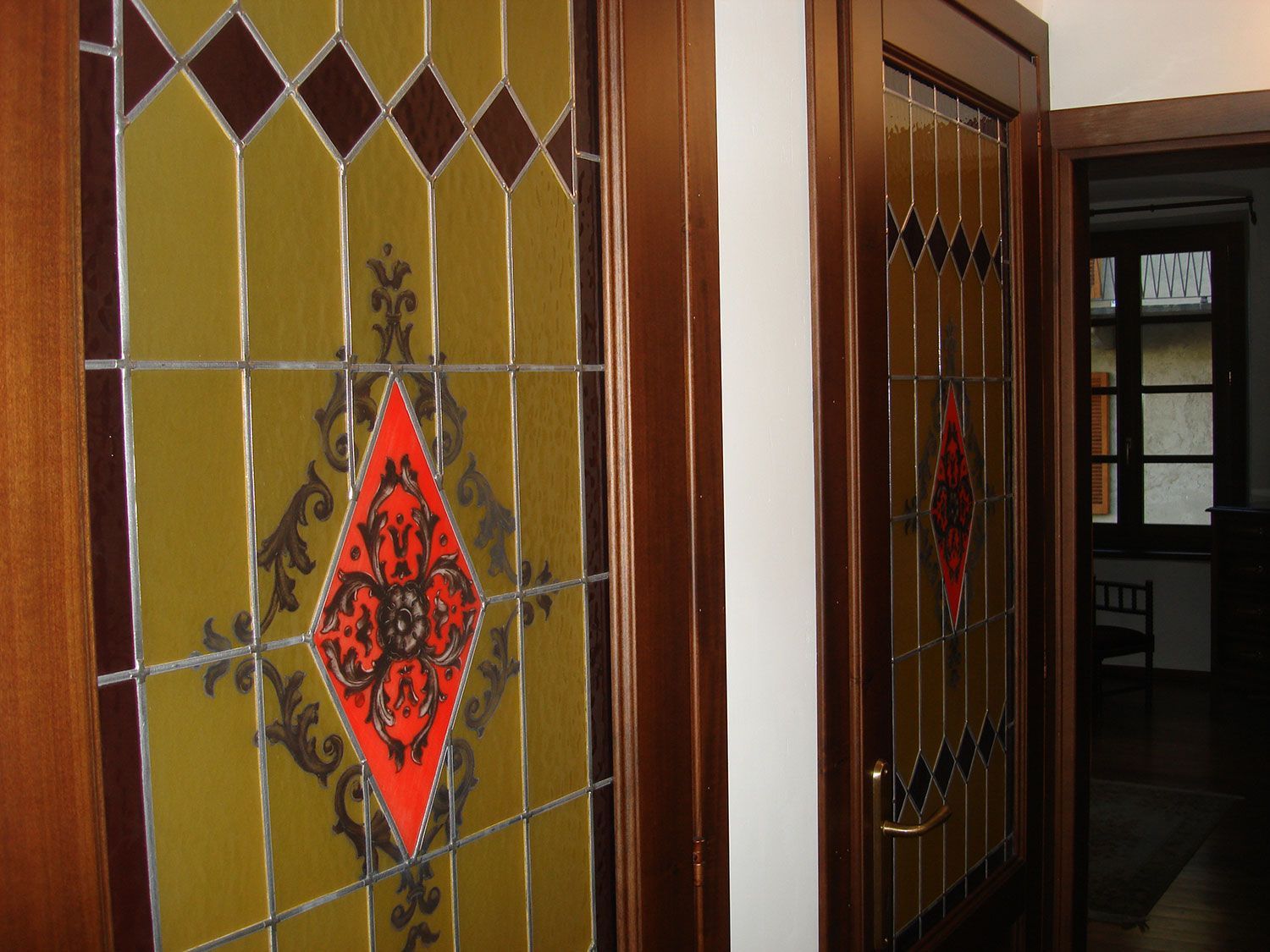 Due porte in legno con pannelli in vetro colorato, caratterizzati da motivi a rombi e floreali nei colori rosso, marrone e giallo.