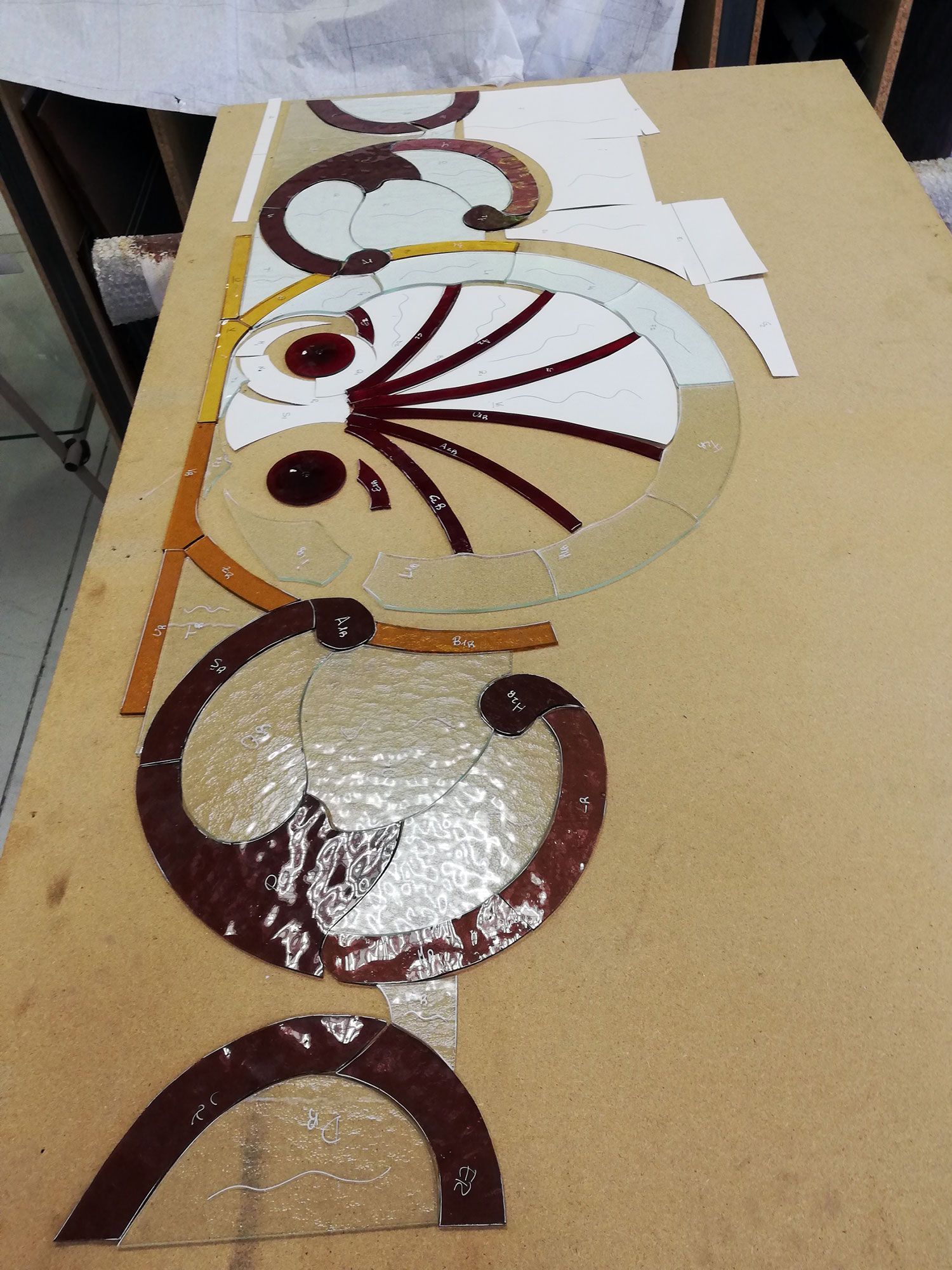 Pezzi di vetro disposti su una superficie di legno, a formare un motivo a mosaico con colori marrone, bianco e oro.