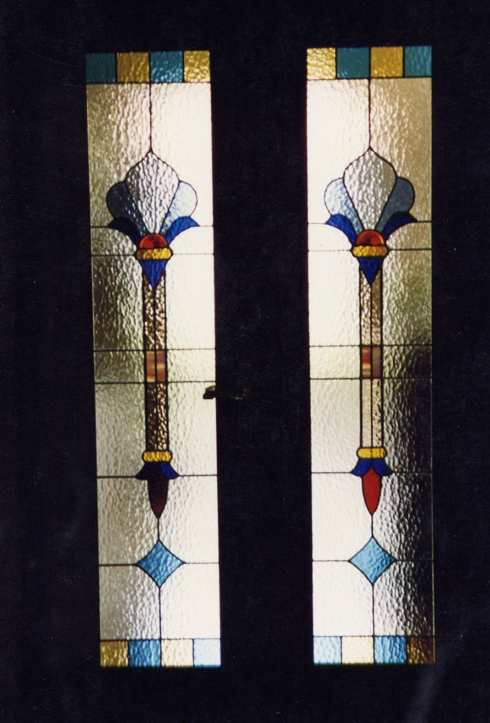 Due pannelli di vetro colorato con elaborati motivi floreali verticali in blu, rosso, oro e vetro trasparente.