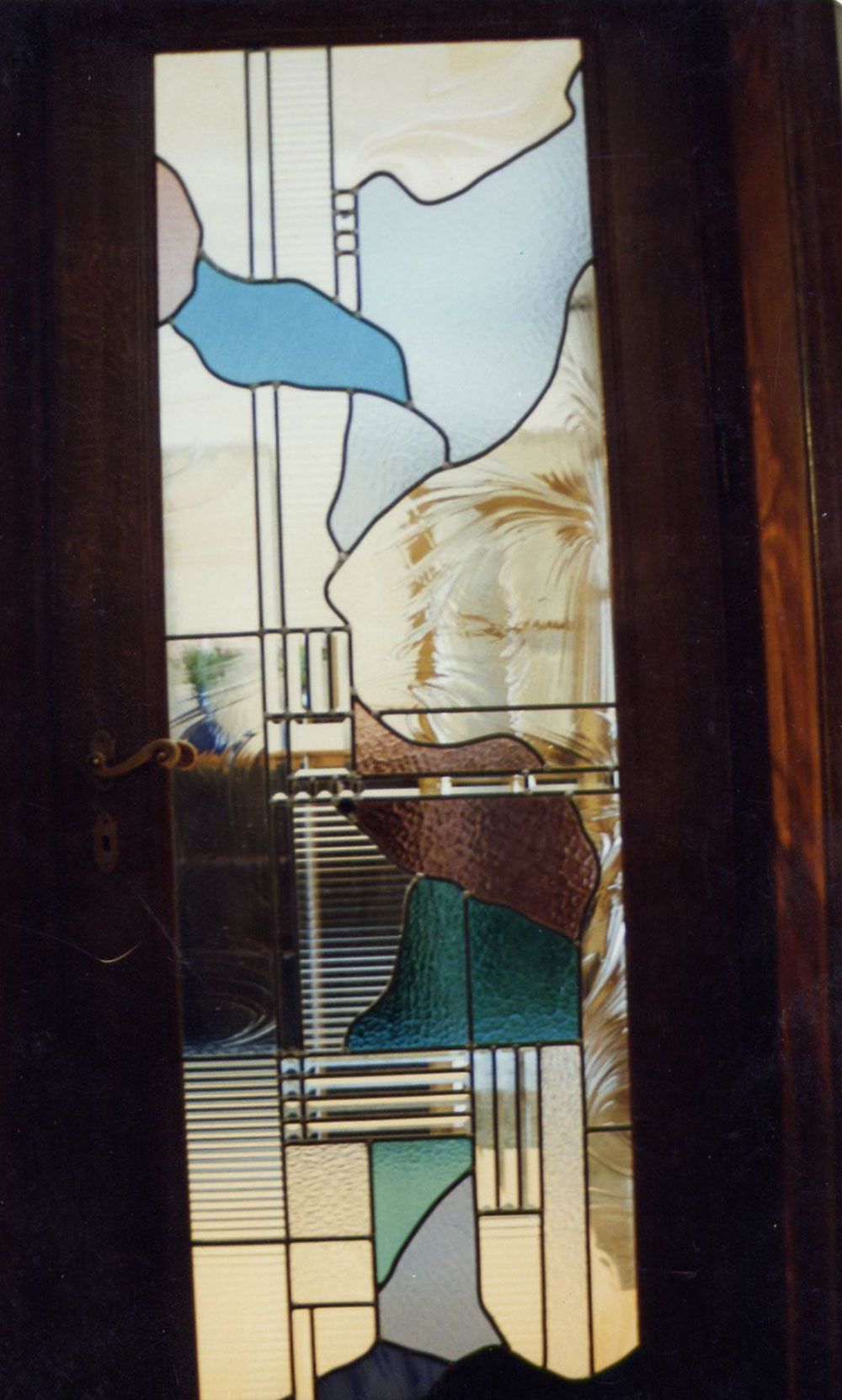 Pannello di porta in vetro colorato con forme astratte in blu, verde, marrone e rosa, incorniciato da una porta in legno scuro.