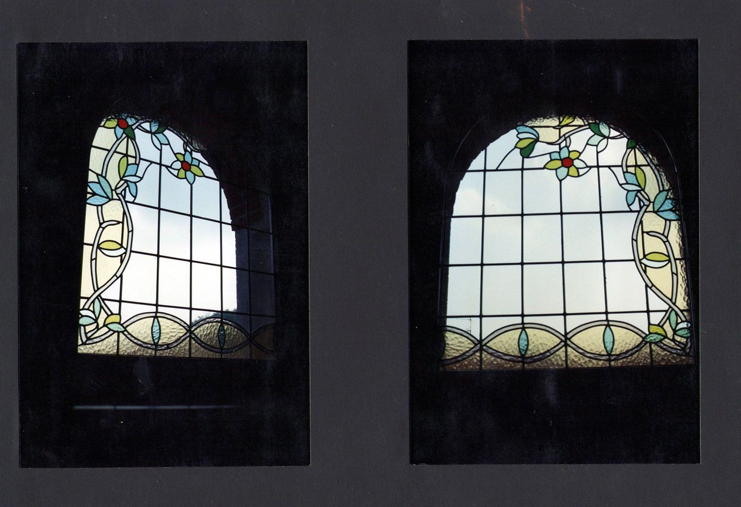 Due finestre ad arco con vetrate colorate e motivi floreali, contro una parete scura.