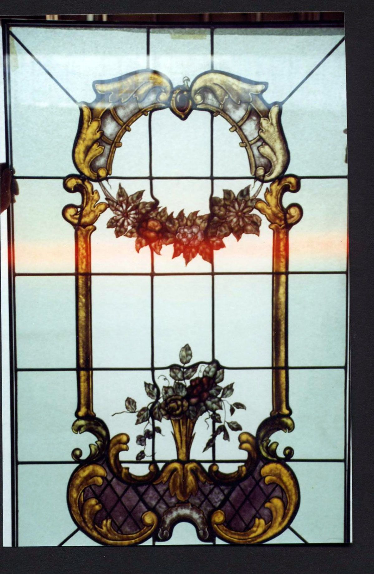 Vetrata con motivo floreale raffigurante un vaso, una ghirlanda e ornati bordi dorati.