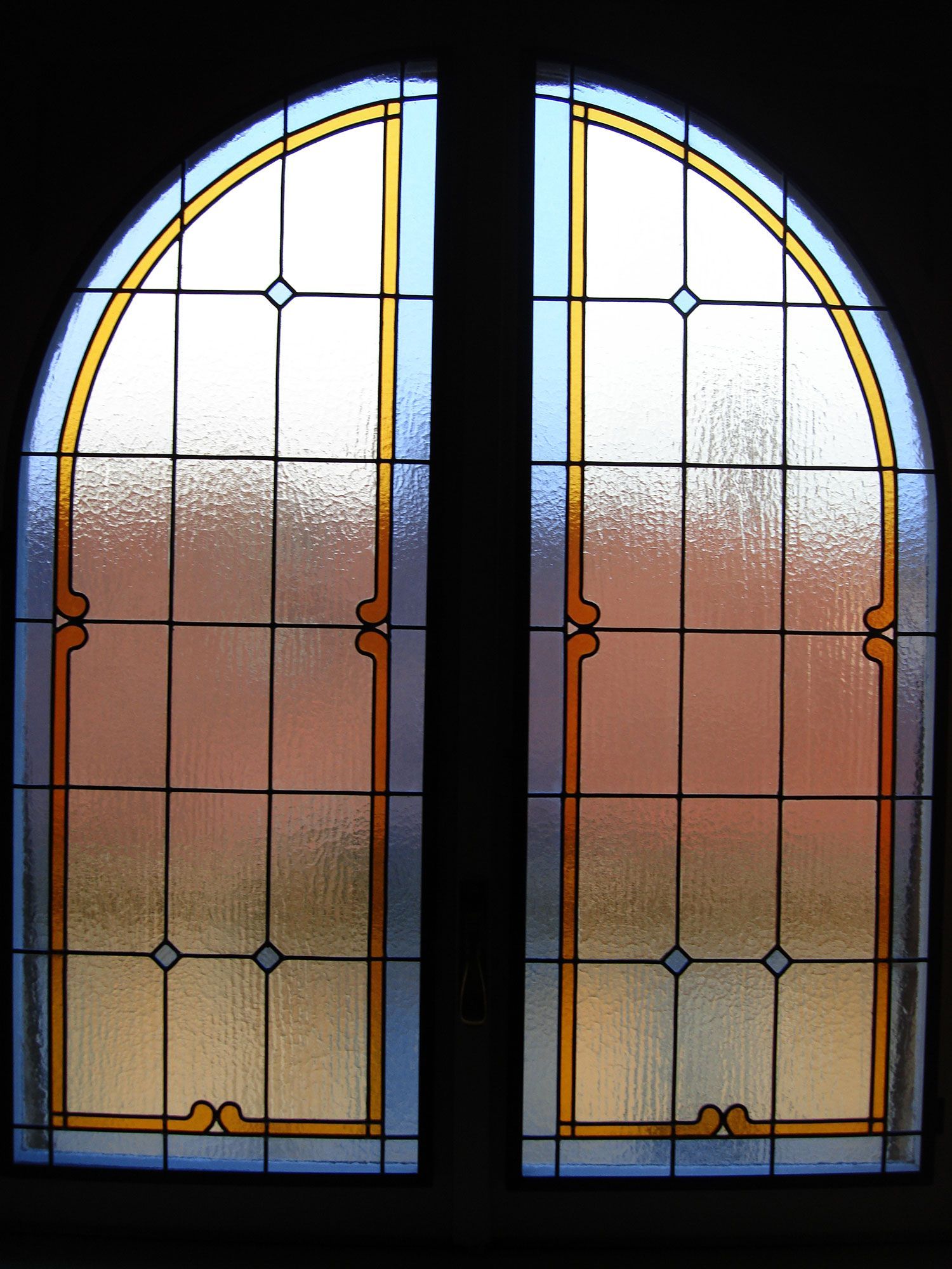 Vetrata con parte superiore arrotondata, divisa in riquadri da linee nere e finiture dorate.