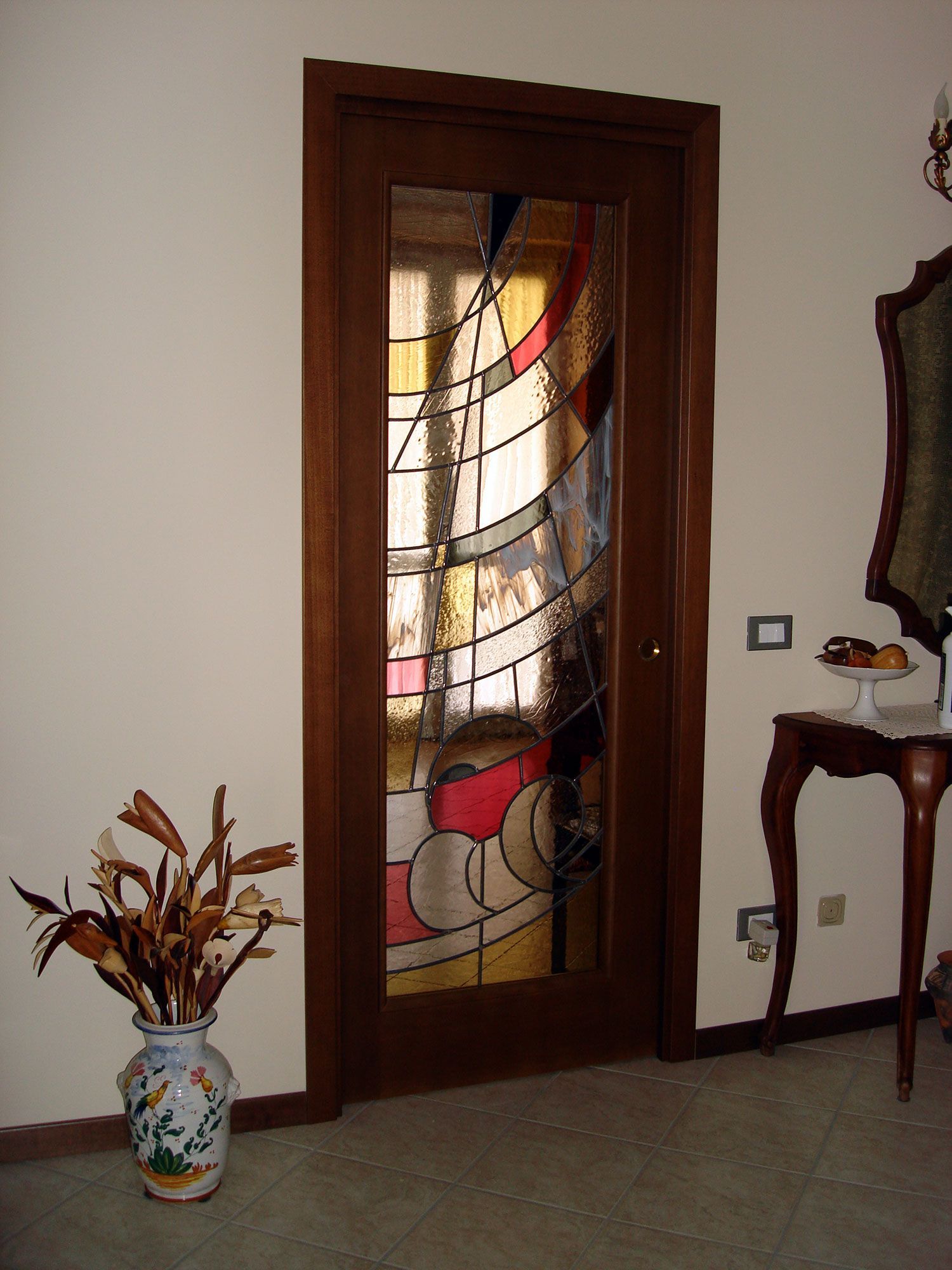 Porta in legno con pannello in vetro colorato, disegno astratto di forme rosse, nere e gialle.