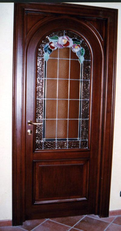 Porta in legno con pannello in vetro arcuato, fiori decorativi e pannello inferiore in legno. Tonalità del marrone.