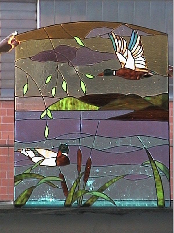 Pannello di vetro colorato raffigurante una scena in uno stagno con anatre: anatre, acqua, canne e nuvole, in vari colori.