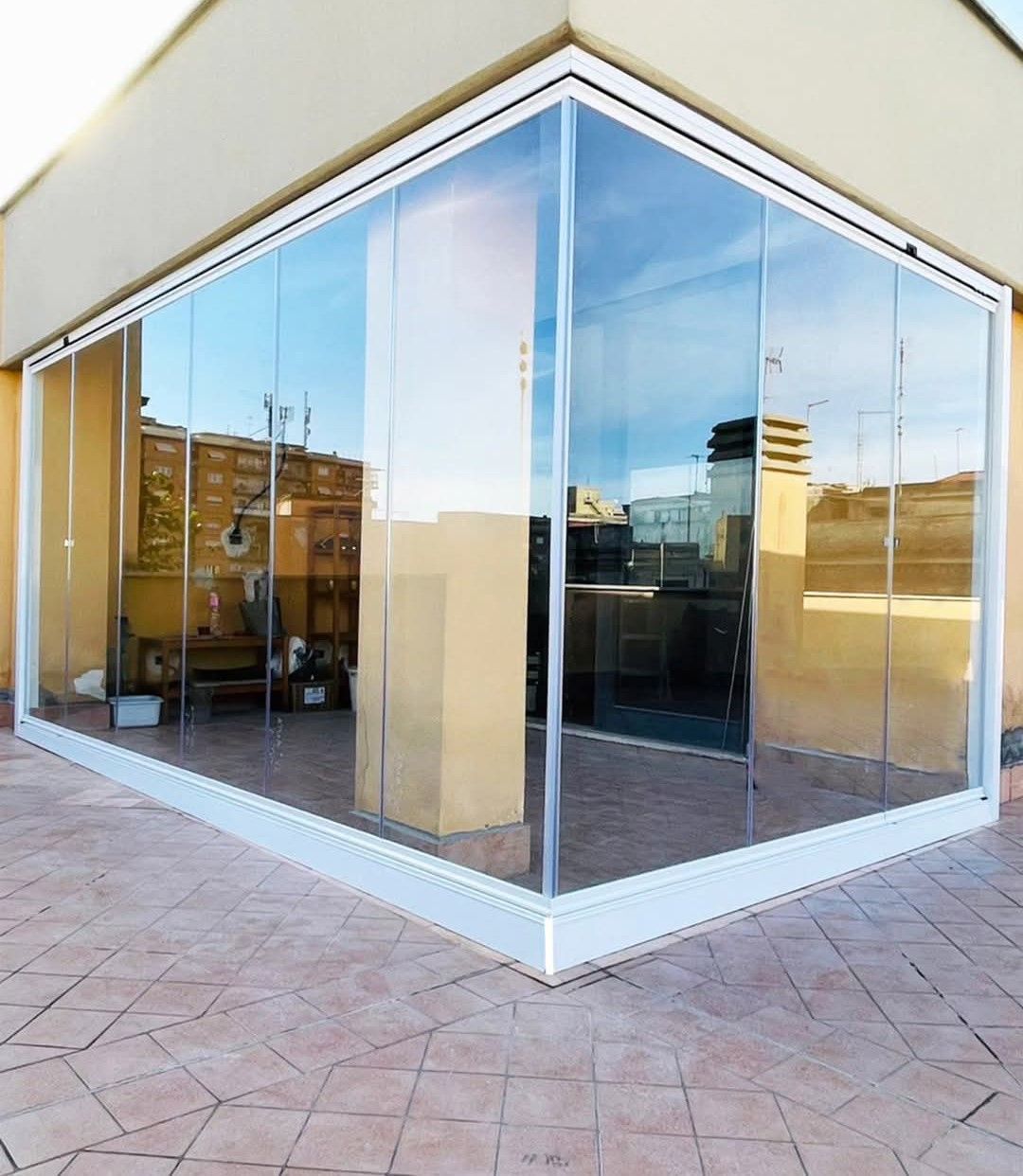 Patio esterno con vetrate e cornice bianca, con vista sul paesaggio urbano.