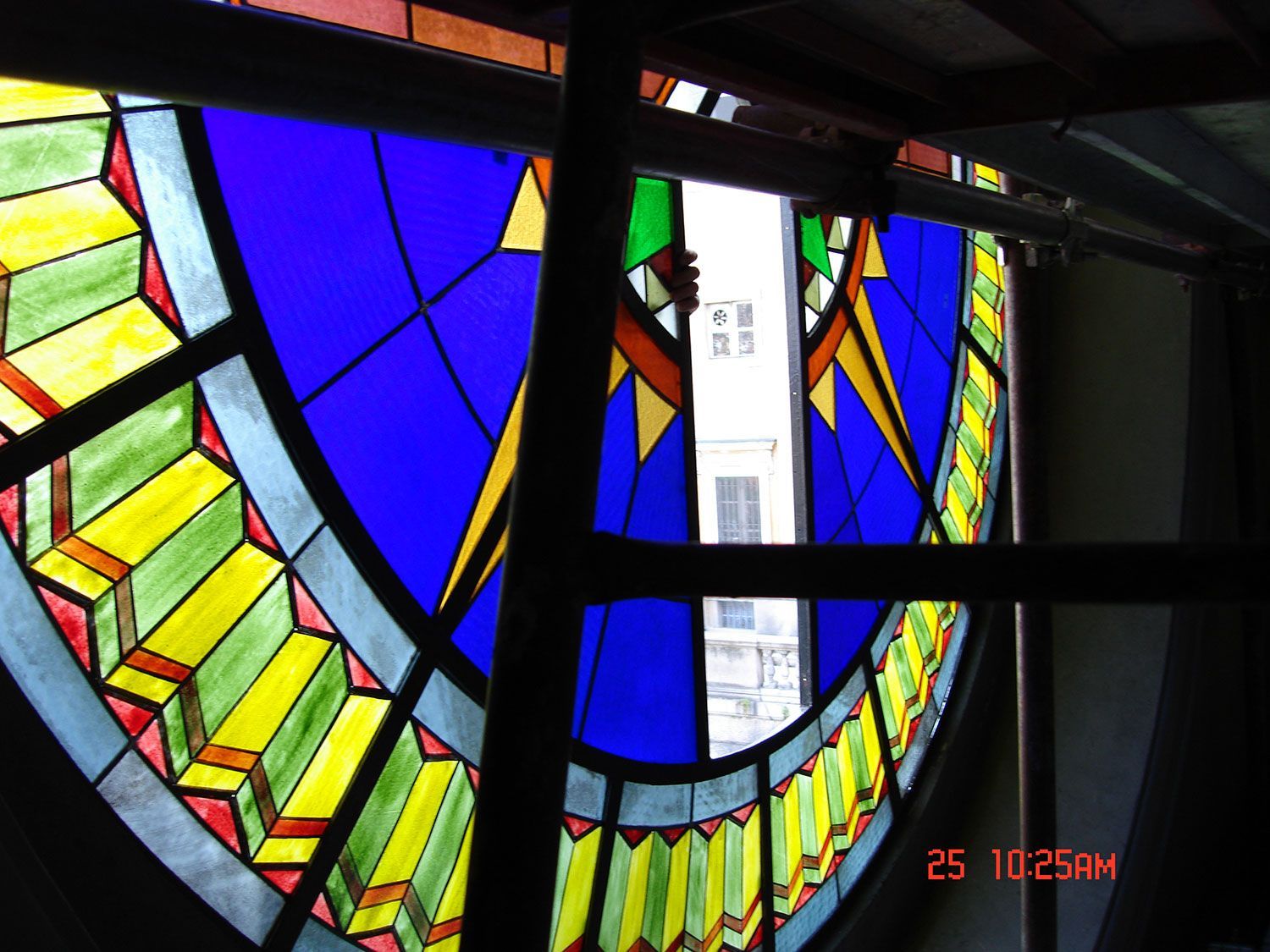 Vetrata con motivi geometrici blu, gialli e verdi; sostenuta da una cornice metallica; vista esterna.