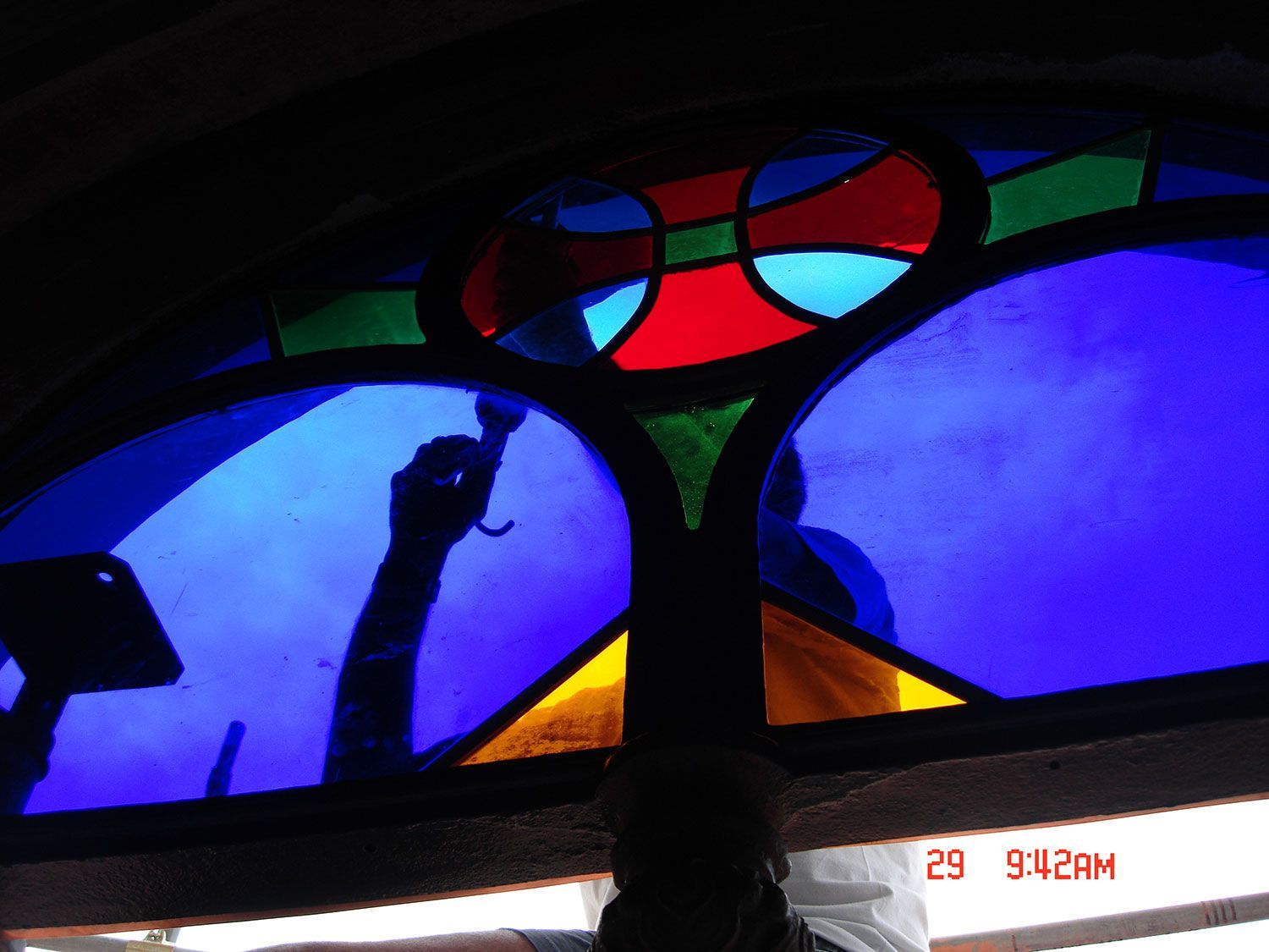 Vetrata con forme blu, rosse e gialle; la sagoma di una persona che lavora su di essa.
