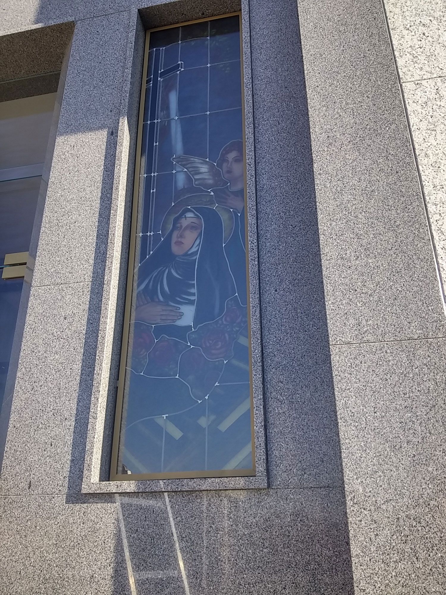 Vetrata raffigurante una donna con un velo nero, forse una suora, insieme ad altre figure; situata in un edificio in pietra.