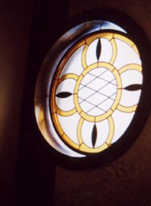 Vetrata rotonda con motivo floreale, inserita in una cornice di legno scuro.