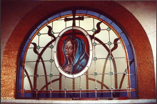 Vetrata: ritratto ovale di una donna con velo blu, arcuato e con una croce sopra.