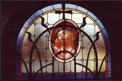Vetrata raffigurante Gesù Cristo con una corona di spine e una croce sopra, in una cornice ad arco.