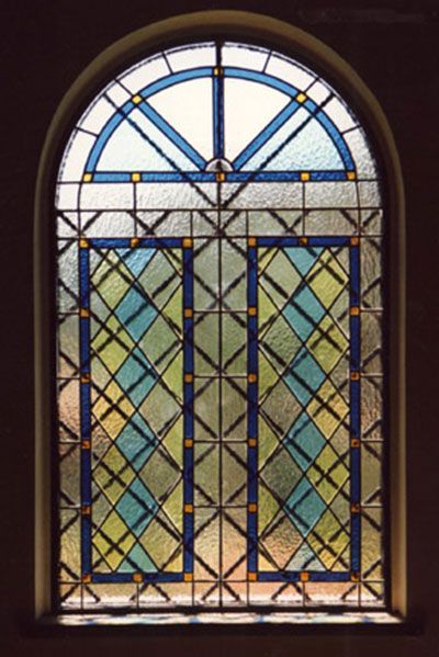 Vetrata ad arco: motivo a rombi blu, gialli e verdi con rifiniture blu e sezione superiore bianca.