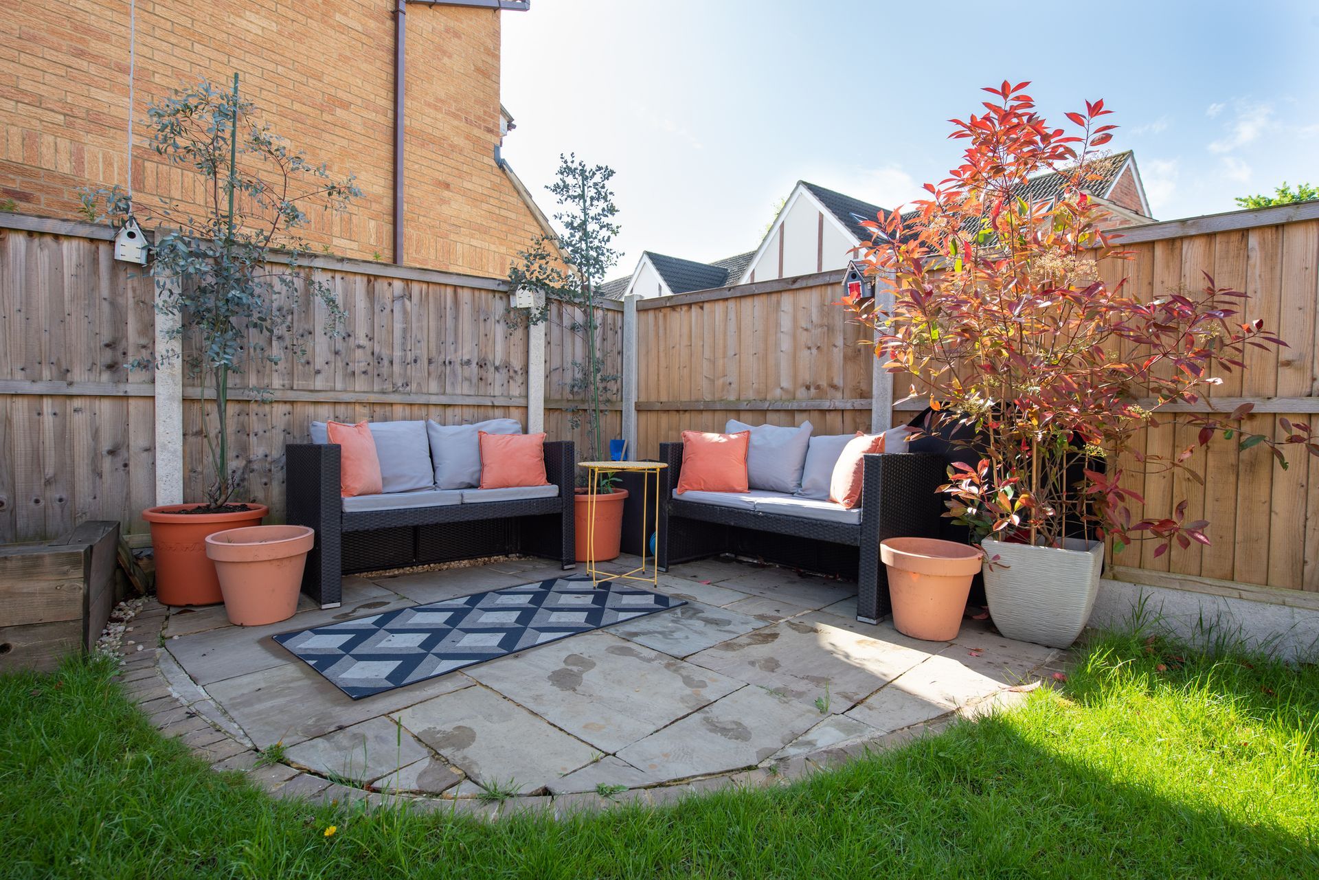 A patio with a couch , table , and potted plants in a backyard.