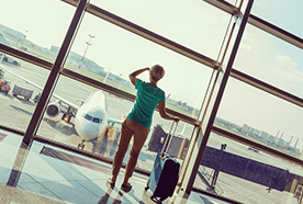 A lady with a wheelie suitcase, looking out of an airport window at a plane standing outside