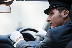 A uniformed chauffeur at the wheel of a car