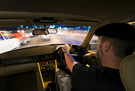 Man in a flat cap driving a car at night