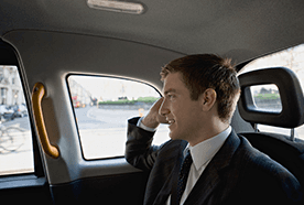 A man in a dark suit and tie, in the back of a car