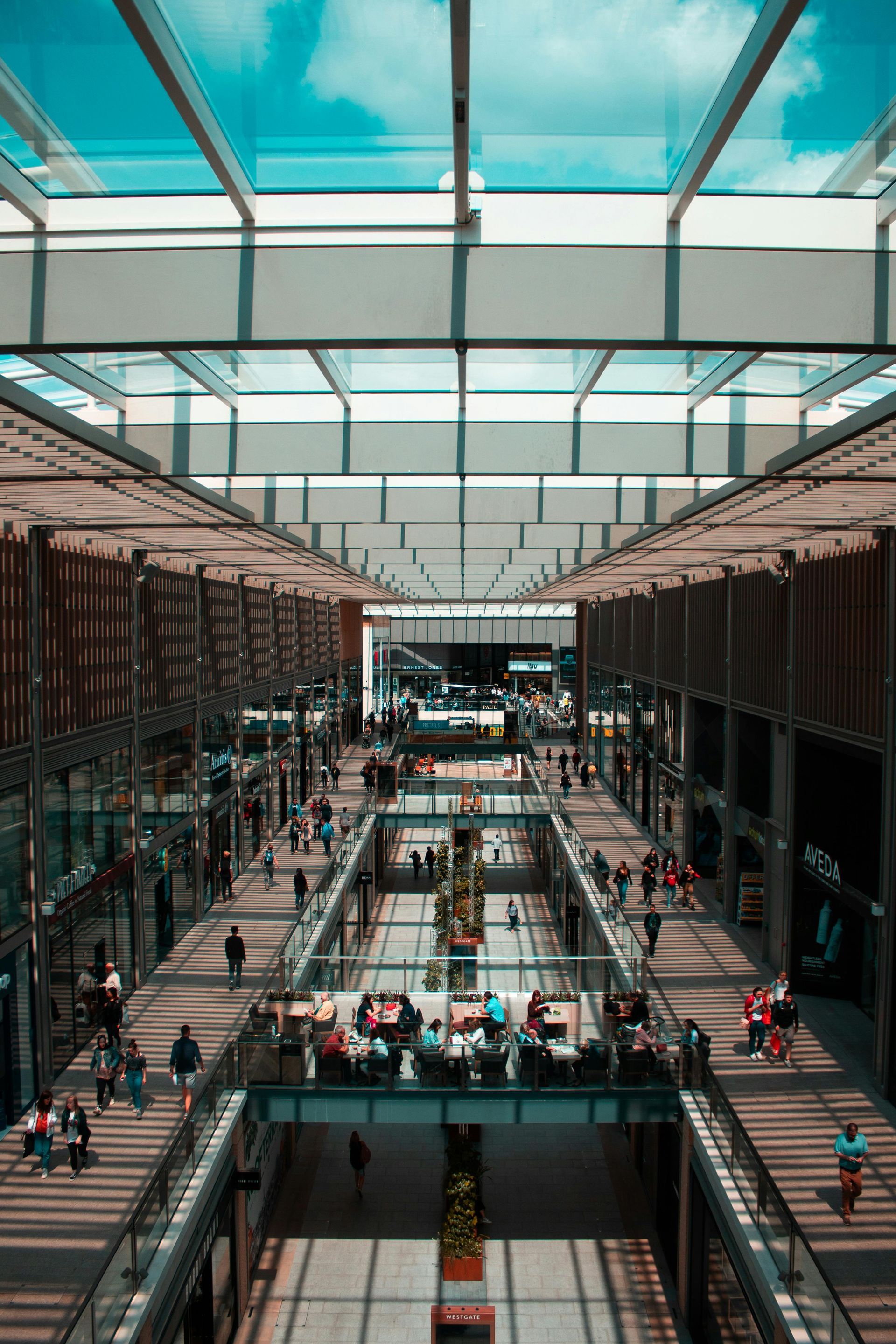 Modern atrium with glass roof, escalators, and crowds walking on multiple levels