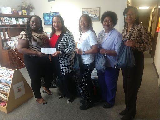 Five women in a room; one holding a check, smiles. Bookstore setting with bookshelves and display.